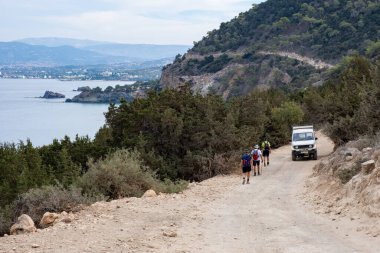 Akdeniz kıyısında tozlu bir off-road yolunda yürüyüş yapan bir grup insan Cyshore sahillerinde doğa ve maceranın tadını çıkarıyorlar.