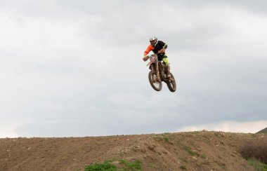 Motokros sürücüsü arazi motorunu off-road pistinin üzerinde fırlatıyor, hava yoluyla hareket ediyor ve bulutlu bir gökyüzü altında ham hız, adrenalin dolu bir yarışma. Açık havada ekstrem sporlar