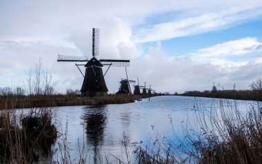 Kinderdijk yel değirmenleri bulutlu gökyüzüne karşı sakin bir kanal boyunca dururlar. Unesco Dünya Mirası Hollanda 'nın ünlü simgesi