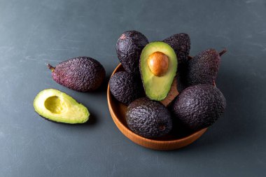 Koyu, olgun avokadolar ahşap bir kâse içinde kırsal yeşil bir yüzey üzerinde, yumuşak karamsar aydınlatmayla yakalanmış..