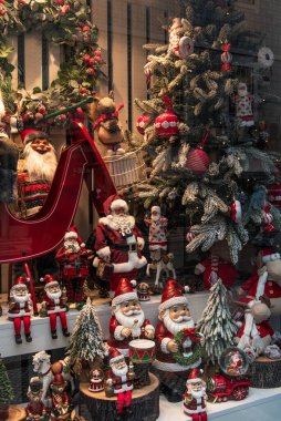 Noel Baba heykelcikleri, Noel süsleri ve süslü Noel ağaçlarıyla dolu bir Noel mağazası penceresi. Sıcak kış atmosferi geleneksel kırmızı ve yeşil renkler, mevsimlik dekorasyonlar, ve sıcak aydınlatma, tatil için ideal, perakende, ünlü
