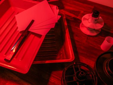 Analog fotoğrafçılık için ekipman, geliştirme tepsisi, fotoğraf kağıtları, tepside bir çift maşa. karanlık oda.