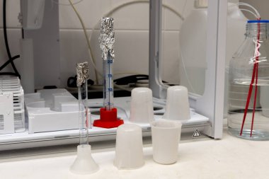 Laboratuvar ekipmanları. Plastik şişeler, cam ölçüm silindirleri ve beyaz masada otomatik yükseltici..