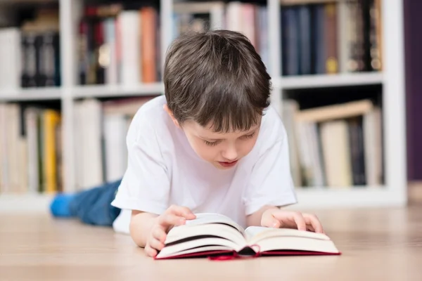 Jongen ligt op zijn buik en het lezen van een boek in de bibliotheek — Stockfoto