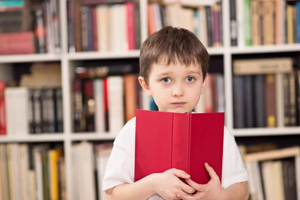 Liten pojke döljer ansiktet bakom boken — Stockfoto
