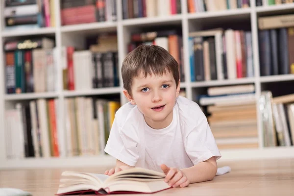 Glad liten pojke läser en bok hemma. — Stockfoto