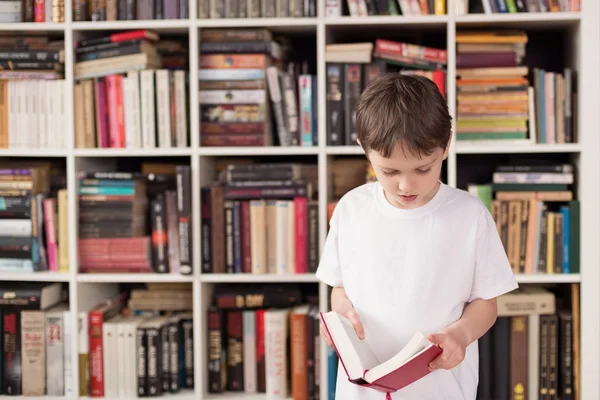 Kleiner Junge steht vor Bücherregal und liest — Stockfoto