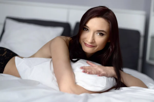 Mulher posando na cama com roupa de cama branca — Fotografia de Stock