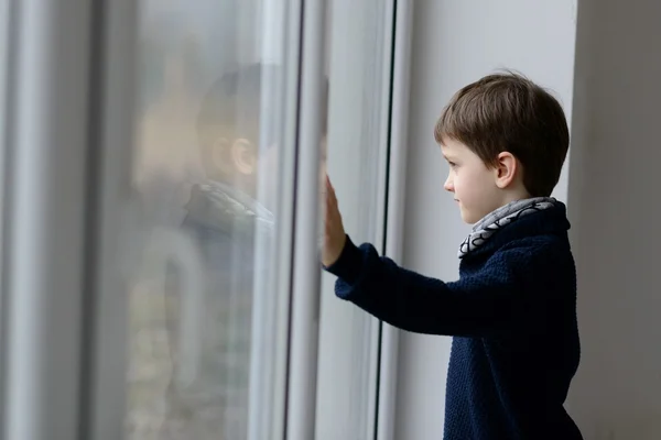 Задумчивый 7-летний мальчик стоит у окна . — стоковое фото