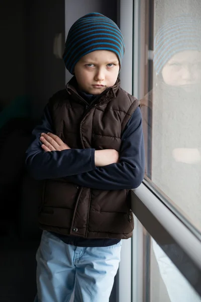 Tersinggung 7 tahun anak laki-laki berusia berdiri di dekat jendela — Stok Foto