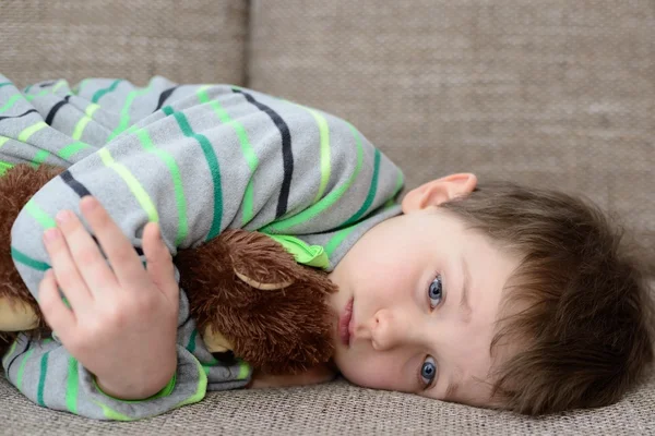 Niño abraza a su osito de peluche y acostado en el sofá — Foto de Stock