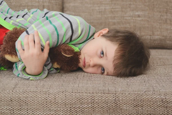 Garçon étreint son ours en peluche et couché sur le canapé — Photo