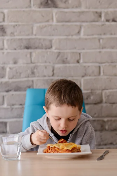 7 anos de idade menino comendo lasanha na sala de jantar — Fotografia de Stock