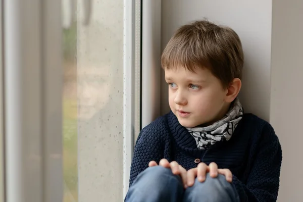 Nachdenklicher kleiner Junge sitzt auf der Fensterbank — Stockfoto