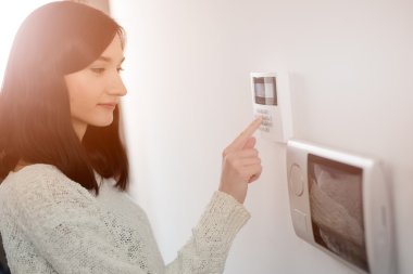 woman entering code on keypad of home security alarm clipart