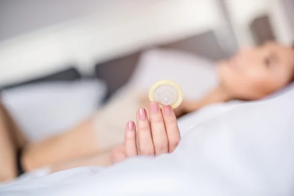 Sexy kobieta w łóżku jest trzymając prezerwatywę na bezpieczny seks. — Zdjęcie stockowe