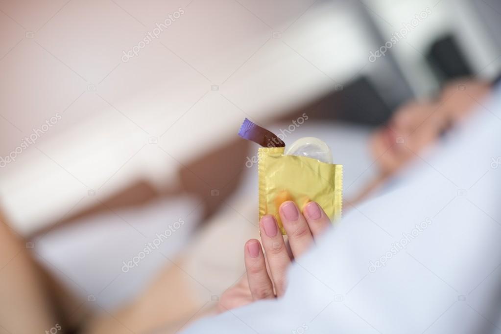 Sexy woman in bed is holding a condom packet