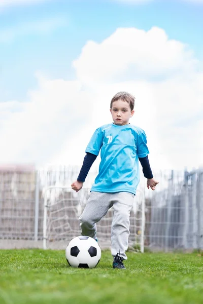 7-летний мальчик пинает мяч в саду . — стоковое фото