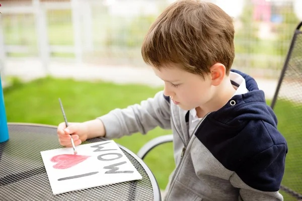 Μικρό παιδί αγόρι ζωγραφική ευχετήρια κάρτα για τη μητέρα του — Φωτογραφία Αρχείου