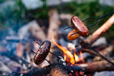 Kamp ateşinin üstünde ızgara sosis.