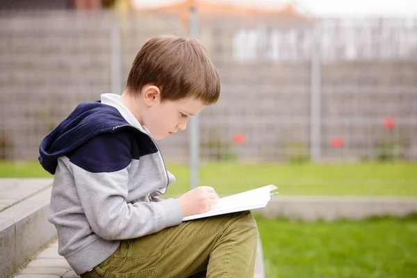 7-jähriger Junge liest ein Buch auf der Terrasse — Stockfoto