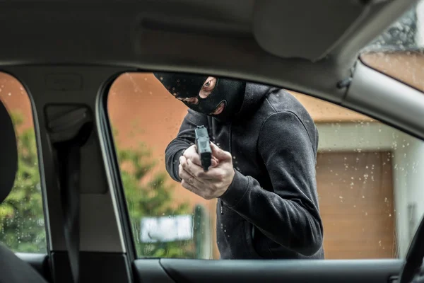 Ladrão de carros apontando uma arma para o motorista — Fotografia de Stock