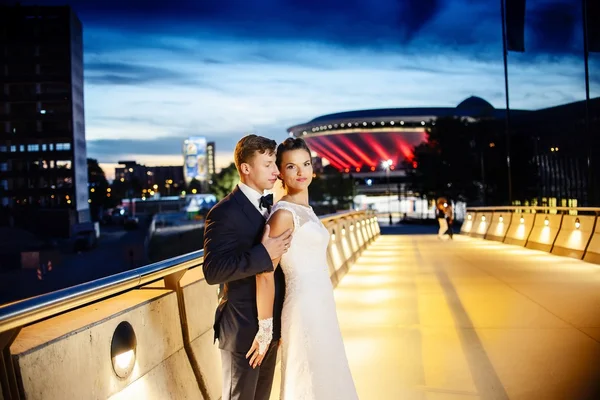 Hermosos recién casados en el puente de la ciudad por la noche — Foto de Stock