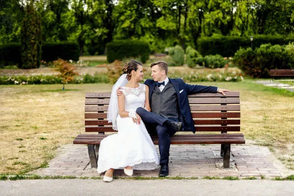 Jeunes mariés assis au banc dans le parc — Photo