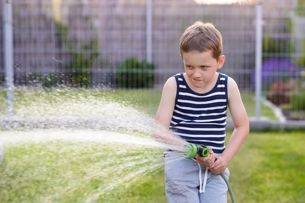 Маленький мальчик поливает траву в саду . — стоковое фото