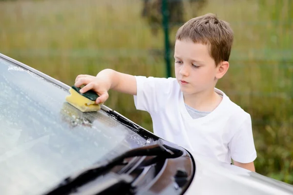 Маленький мальчик моет серебристую машину в саду — стоковое фото
