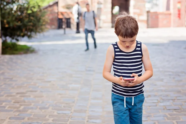 Маленький 7-летний мальчик играет в мобильные игры на смартфоне — стоковое фото