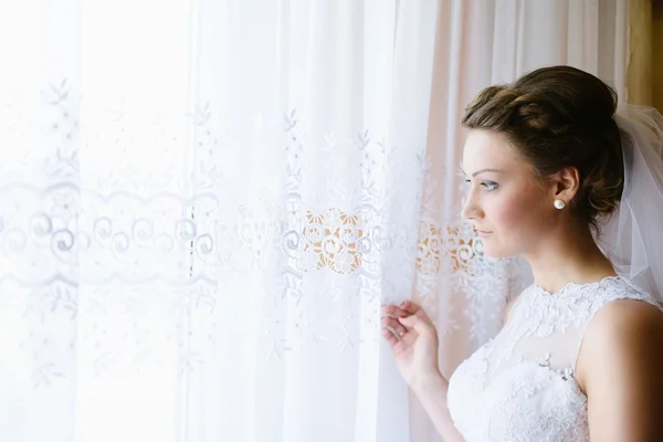 Junge Braut im weißen Kleid schaut aus dem Fenster. — Stockfoto