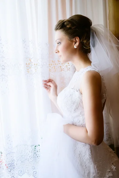 Young bride in white dress looking out the window. — Stock Photo, Image