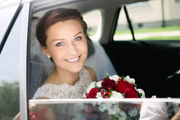 Schöne junge Braut mit Blumenstrauß im Hochzeitsauto — Stockfoto