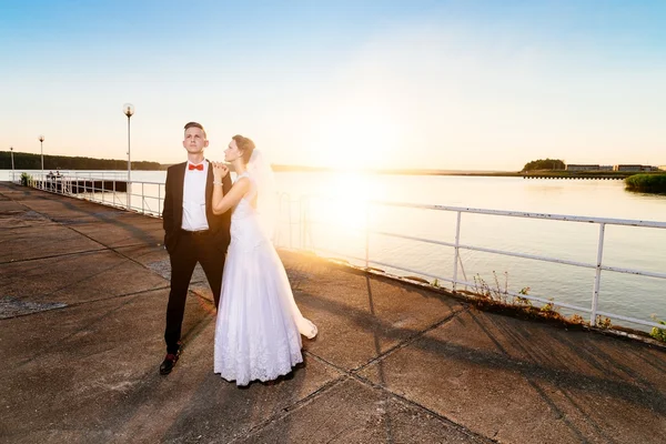 Bride and groom on the pier at sunset. — Stock Photo, Image