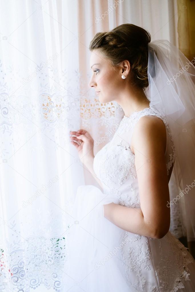 Young bride in white dress looking out the window.