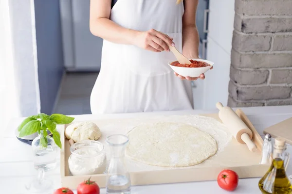 Frau fügt Tomatensauce auf Pizza hinzu — Stockfoto
