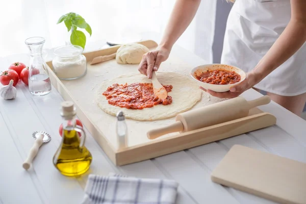 Mujer añadiendo salsa de tomate en la pizza — Foto de Stock