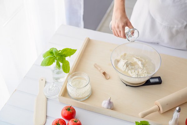 Женщина добавляет воду в муку в миске
.