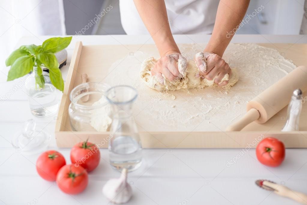 Woman kneading pizza dough on wooden pastry board
