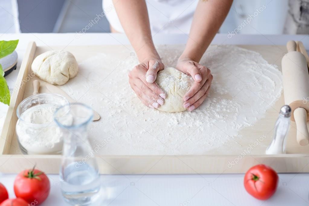 Woman kneading pizza dough on wooden pastry board