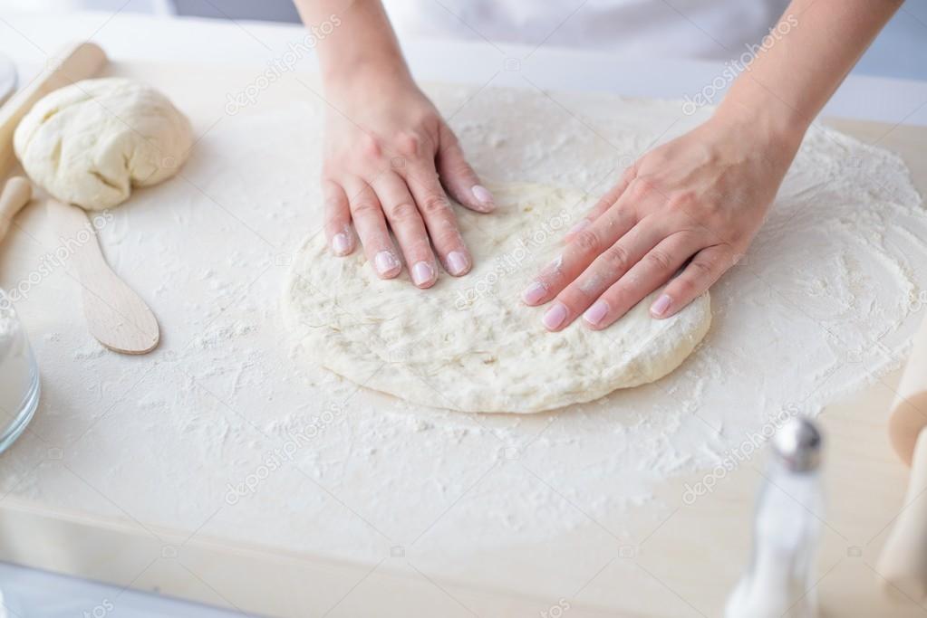 Woman kneading pizza dough on wooden pastry board.