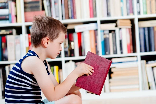 Siebenjähriger Junge liest in Bibliothek ein Buch. — Stockfoto