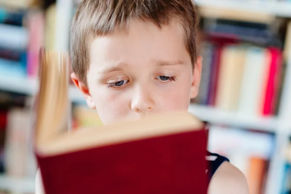 Sedm let starý chlapec s knihou v knihovně. — Stock fotografie