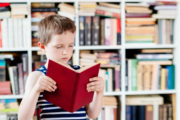 Sedm let starý chlapec s knihou v knihovně. — Stock fotografie