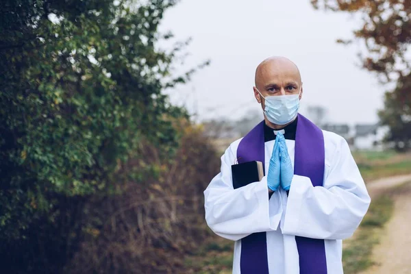 Yolda bir yerlerde koruyucu maske ve koruyucu eldivenler takmış dua eden bir rahip. — Stok fotoğraf