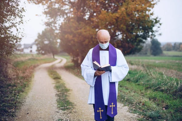 Молодой священник читает Святую Библию в поле — стоковое фото