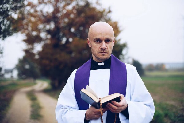 Catholic priest reading bible on a country road