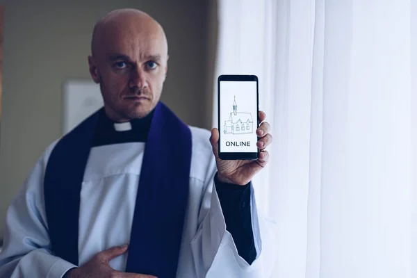 Hombre sacerdote sosteniendo un teléfono celular con información sobre las reuniones de la iglesia en línea — Foto de Stock