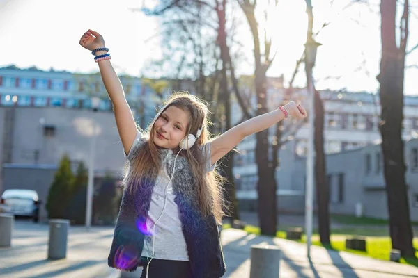 Una niña de 10 años con las manos en alto y auriculares en las orejas —  Fotos de Stock
